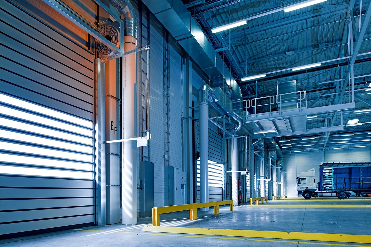 A modern warehouse interior illuminated by fluorescent lights, featuring loading docks and a parked delivery truck.